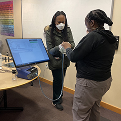 Person hands a face mask to another person. Mask is linked to a machine with a computer monitor.